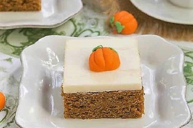 Killer Pumpkin Bars with Cream Cheese Frosting on a white ceramic plate with a candy pumpkin garnish