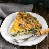 Slice of Crustless Spinach Quiche on a white plate with a bamboo handled fork