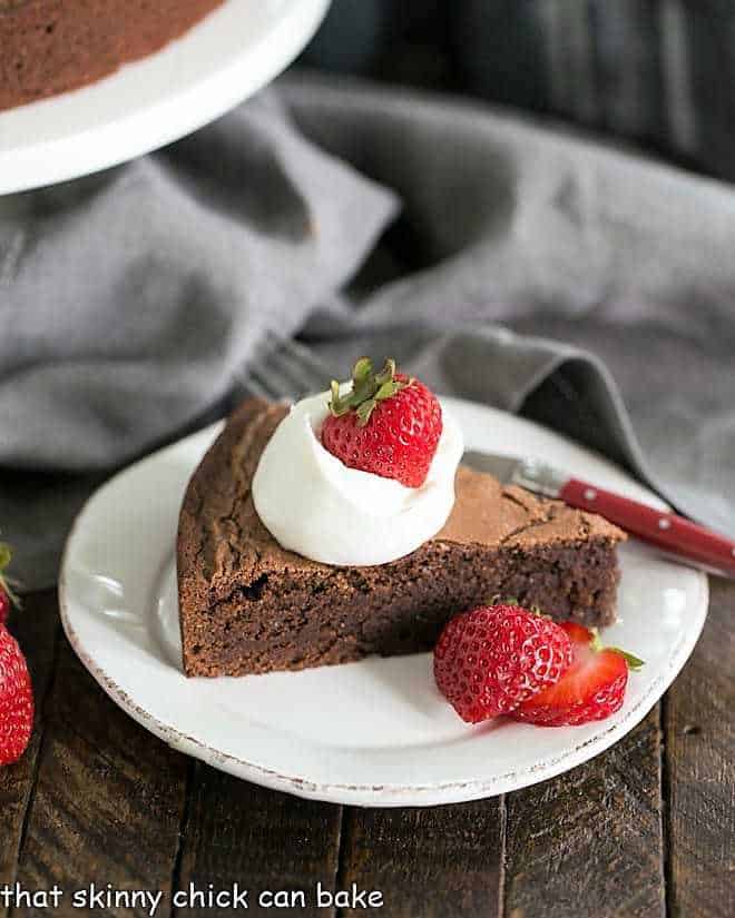 Italian Flourless Chocolate Cake on a white dessert plate with a dollop of cream and strawberries