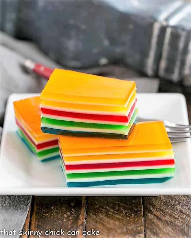 Layered Jello Rainbow Salad squares stacked on a white plate.