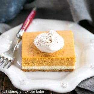 A slice of Layered Pumpkin Cheesecake Bars topped with whipped cream