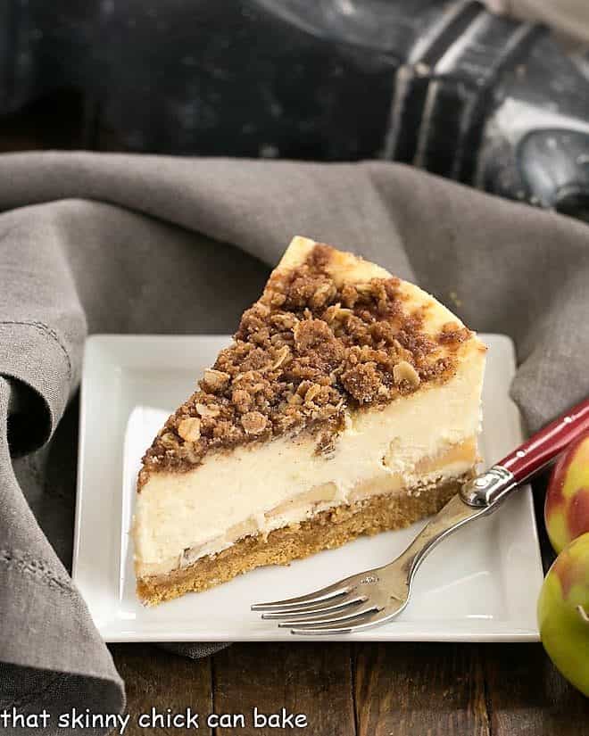 Slice of Apple Crisp Cheesecake on a white plate with a red handled fork