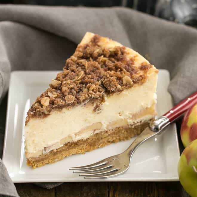 Slice of apple crisp cheesecake on a square white plate