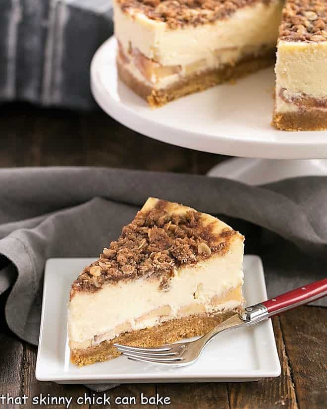 Slice of Apple Crisp Cheesecake in front of cake stand.