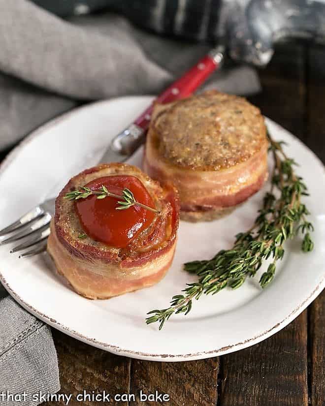 Two bacon wrapped meatloaf muffins on a round white plate