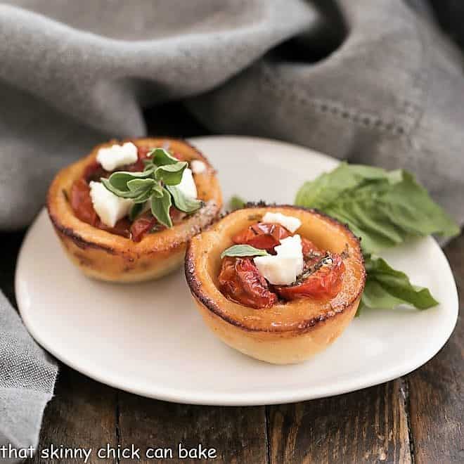 Cheese Straw Tomato Tartlets on an oval white plate with a sprig of basil