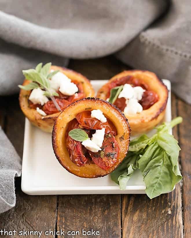 Buttery, cheesy pastry crusts filled with herb marinated tomatoes and feta cheese for an irresistible appetizer Cheese Straw Tomato Tartlets on a square white plate.