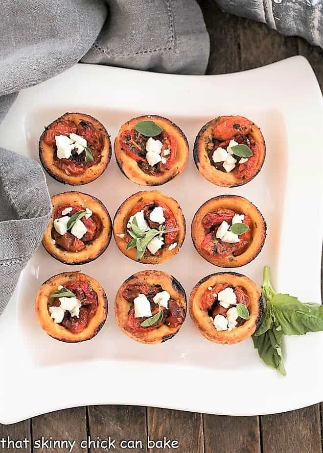 Buttery, cheesy pastry crusts filled with herb marinated tomatoes and feta cheese for an irresistible appetizer Cheese Straw Tomato Tartlets on a white serving tray.