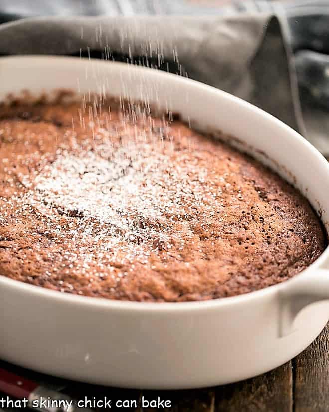 Self saucing chocolate pudding cake in an oval casserole dish dusted with powdered sugar.