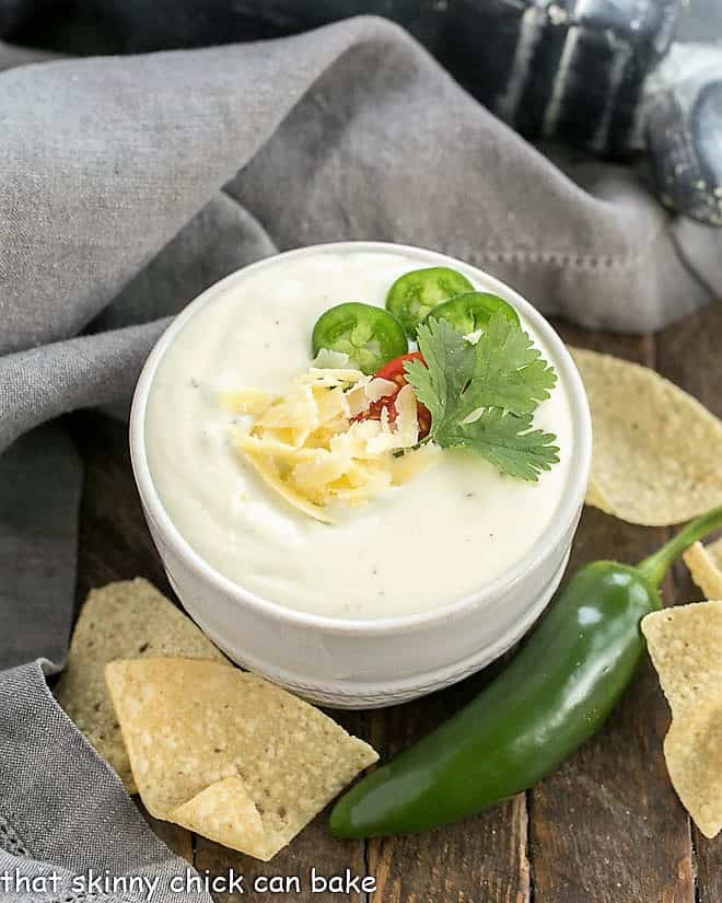 Small white bowl of Easy Homemade Queso Dip garnished with cheese and cilantro.