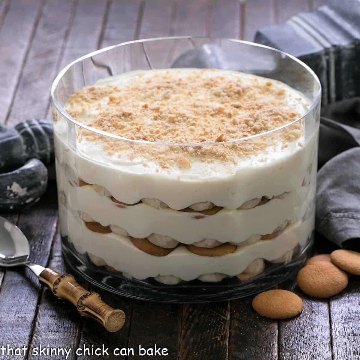 Banana pudding in a glass dish with a serving spoon and vanilla wafer cookies.