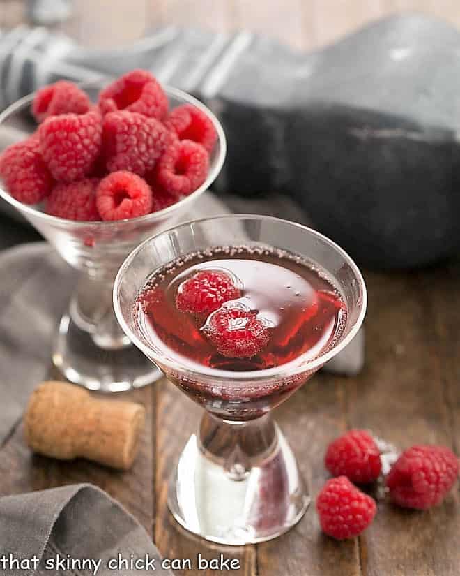 Classic Kir Royale with Cassis in a champagne glass in front of a glass of raspberries.