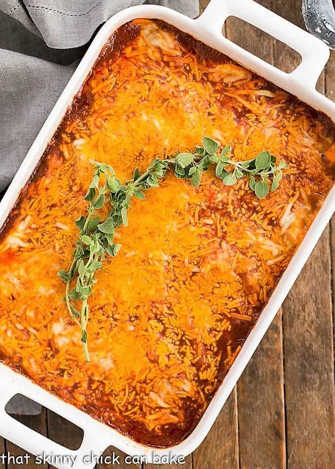 Turkey Enchilada Casserole in a white casserole dish with a sprig of oregano