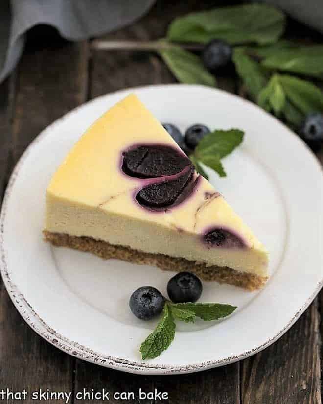 Blueberry Swirl Cheesecake slice on a white plate with mint and fresh blueberries