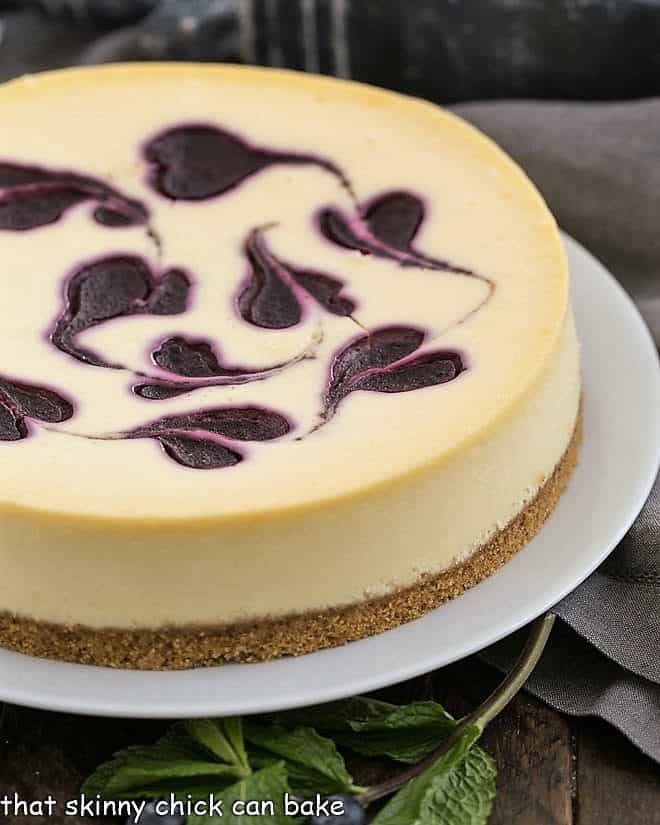 Uncut Blueberry Swirl Cheesecake on a white serving plate.