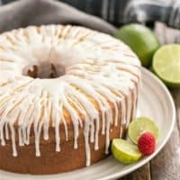 A close up of key lime pound cake on a white serving plate garnished with limes and a raspberry