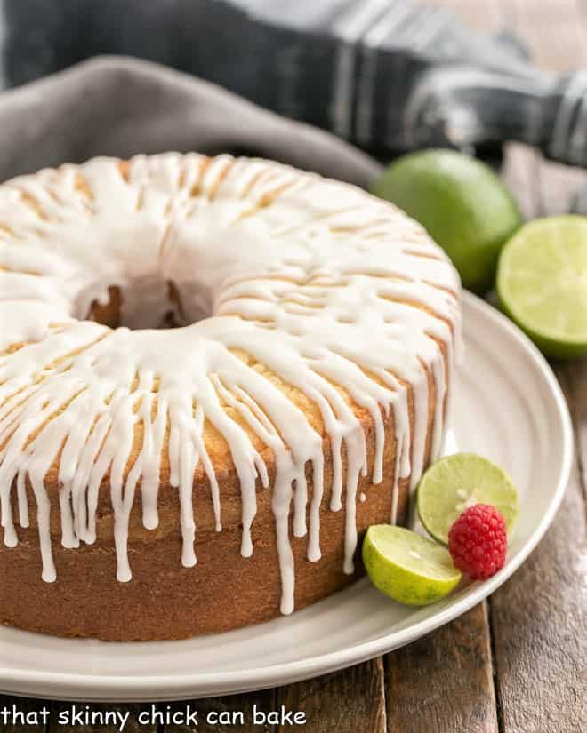 A close up of key lime pound cake on a white serving plate garnished with limes and a raspberry.