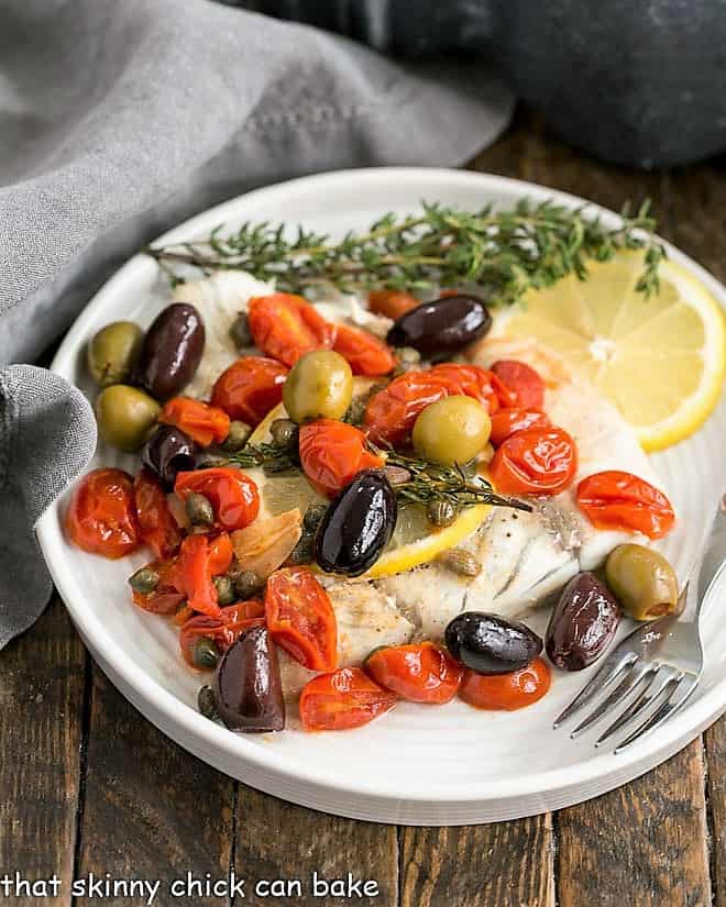 Mediterranean Sea Bass en Papillote on a white dinner plate with a lemon slice and thyme garnish.