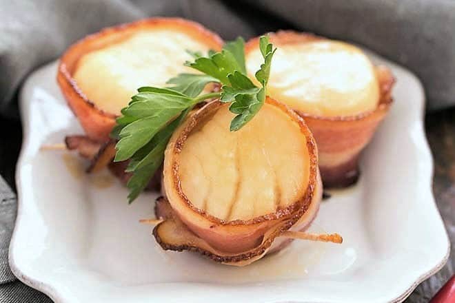 Scallops wrapped in bacon on a white appetizer plate