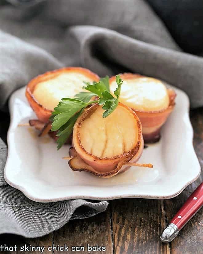 Scallops wrapped in bacon on a white appetizer plate.