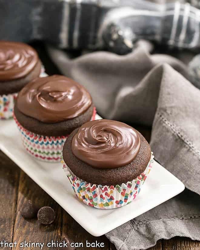 Cream Filled Chocolate Cupcakes lined up on a white ceramic tray.