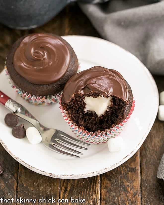Cream Filled Chocolate Cupcakes on a round white plate with one cupcake revealing the cream filling. Better than Hostess copycat recipe!