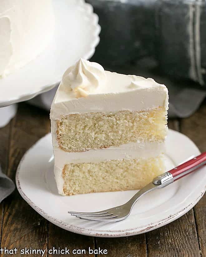 Slice of Classic White Layer Cake with White Chocolate Swiss Meringue Buttercream on a white dessert plate.