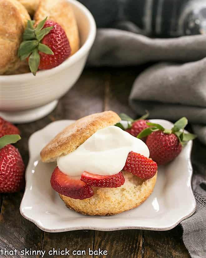 Strawberry Shortcakes with White Chocolate Mousse on a square white plate with a bowl of biscuits in the background.
