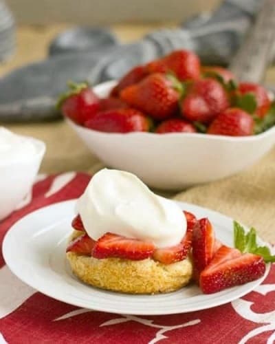 Strawberry Shortcakes with White Chocolate Whipped Cream on a white plate next to a bowl of strawberries
