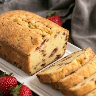 Loaf of Fresh Strawberry Pound Cake on a white ceramic tray with half cut into slices