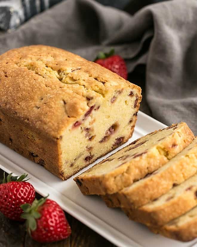 Loaf of Fresh Strawberry Pound Cake on a white ceramic tray with half cut into slices.