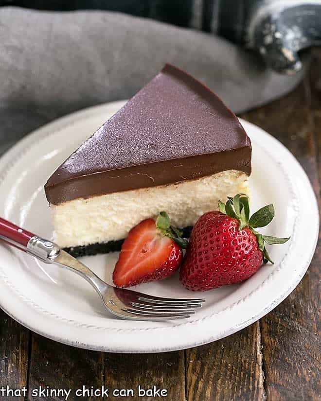 Ganache Topped Cheesecake slice on a white plate with strawberries.