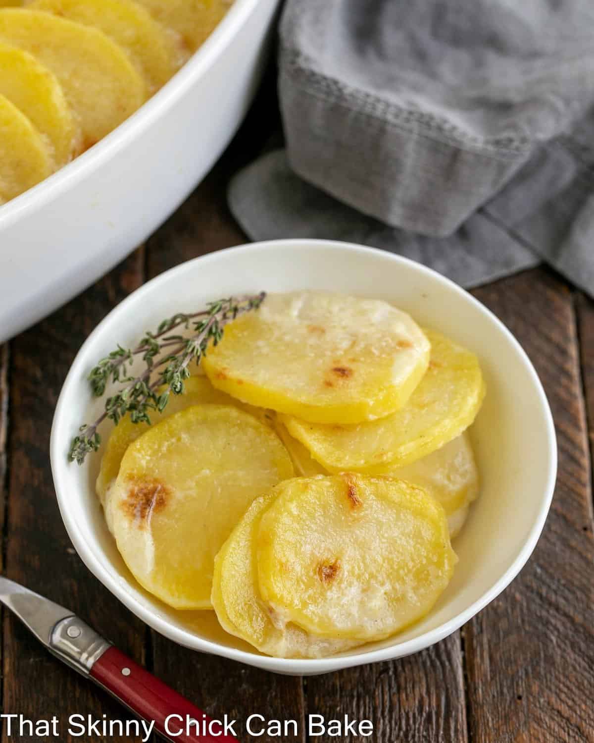 Close view of  a small bowl of scalloped potatoes next to the casserole dish.