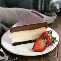 Ganache Topped Cheesecake on a white plate with ripe strawberries to garnish