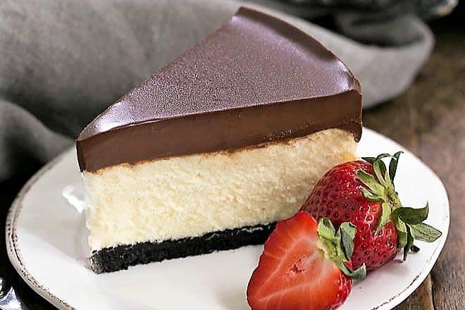 Ganache Topped Cheesecake on a white plate with ripe strawberries to garnish