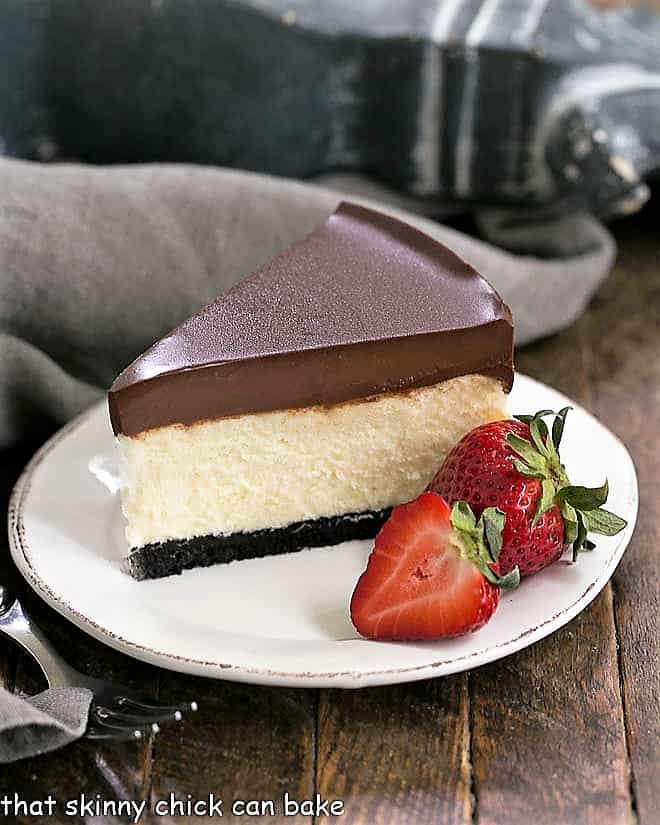 Ganache Topped Cheesecake on a white plate with ripe strawberries to garnish