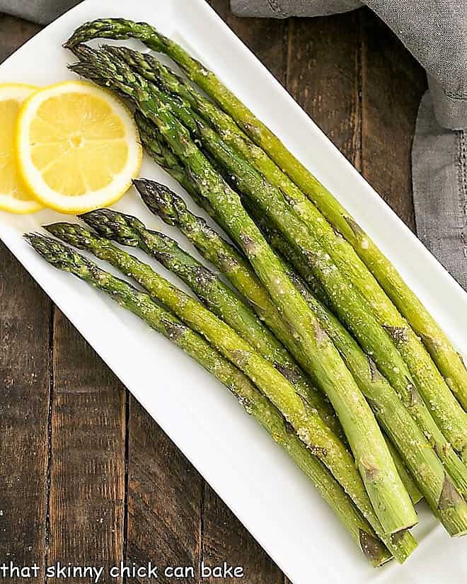 Overhead view of Easy Oven Roasted Asparagus on a white tray with lemon slices.