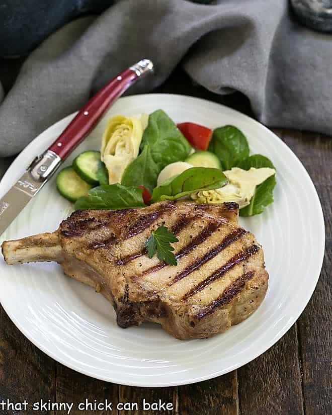 Overhead view of marinated pork chop with a salad on a white plate.