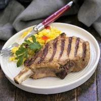 Grilled marinated pork chop on a dinner plate with fresh corn and a red handled fork