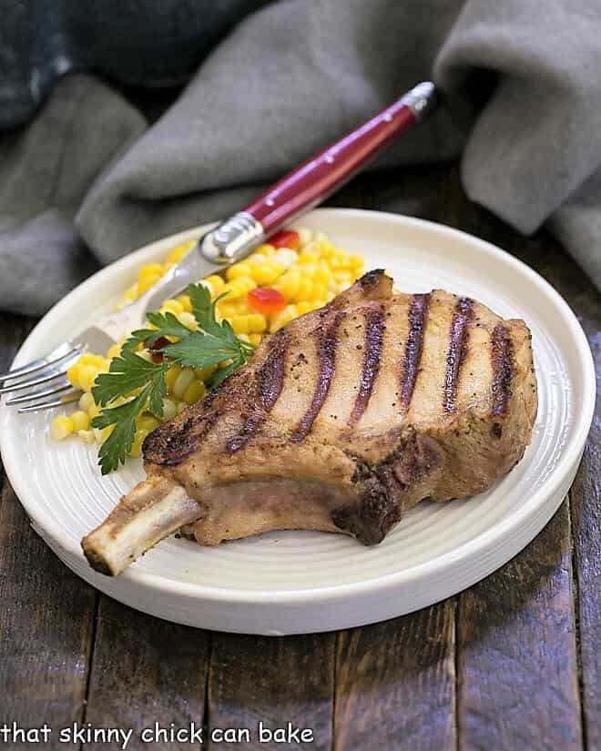 Grilled marinated pork chop on a dinner plate with fresh corn and a red handled fork.