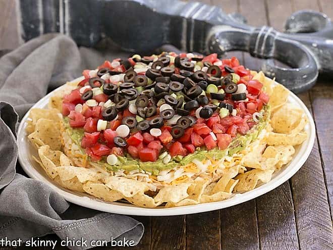 Easy Layered Taco dip on a white serving plate surrounded by tortilla chips.