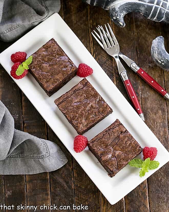 3 sheet pan brownies on a white tray with raspberries and mint.