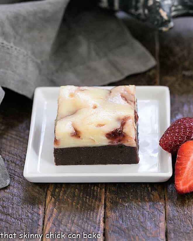 A strawberry brownie on a square white plate with fresh strawberries