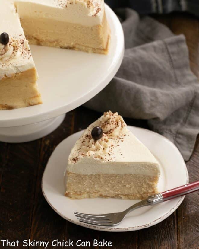 Slice of tiramisu cheesecake on a white dessert plate in front of the remaining cheesecake.