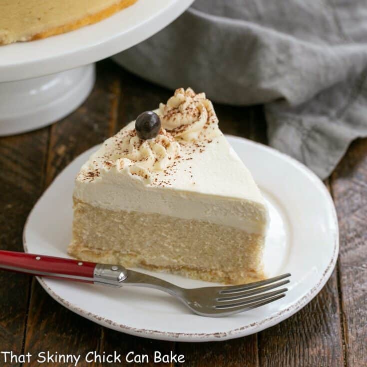 Slice of Tiramisu cheesecake on a white dessert plate with a red handled fork.