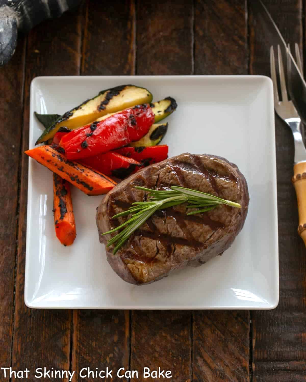 Overhead view of grilled fillet on a white plate with grilled vegetables.