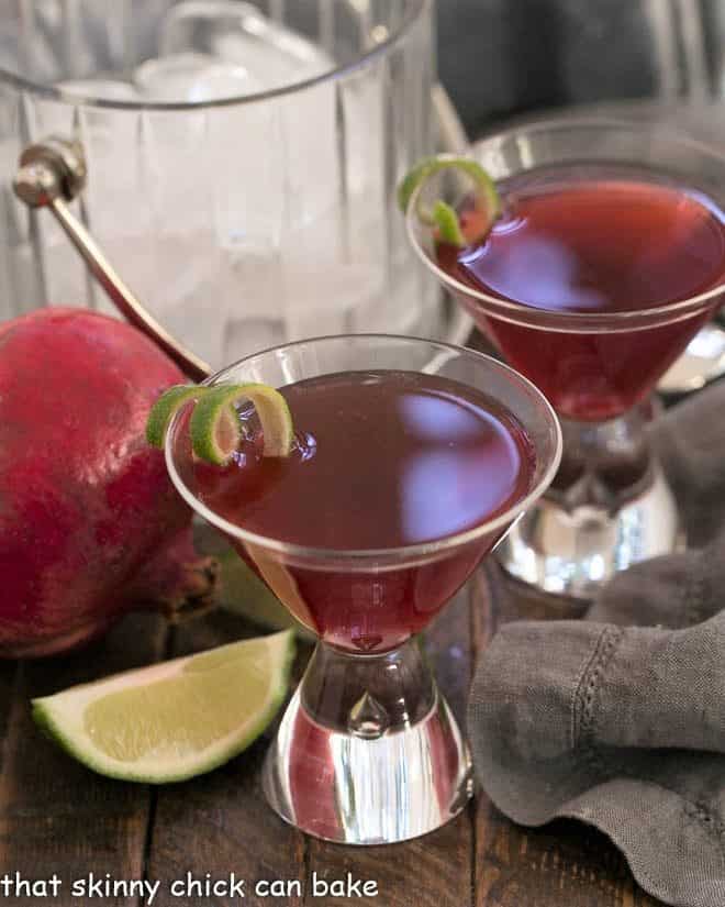 Two Pomegranate Cosmopolitan Cocktails in martini glasses with lime twists.