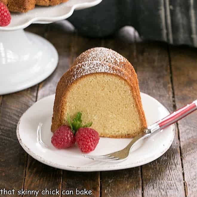 Sour Cream Pound Cake slice on a square white ceramic plate with two raspberries and a sprig of mint with a red fork