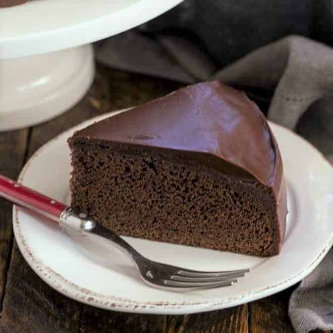 One layer fudge cake on a round white plate with a red handle fork.