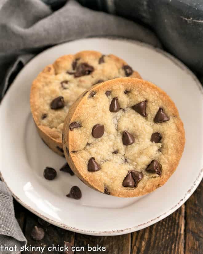 Chocolate Chip Cookie Bar for One - a small batch recipe that bakes up a big chocolate chip cookie in no time!! Overhead view of two chocolate chip cookie bars on a round white plate with some stray chocolate chips.